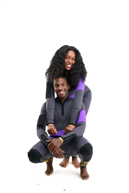 Two people in matching wetsuits posing together happy squat pose on a white background